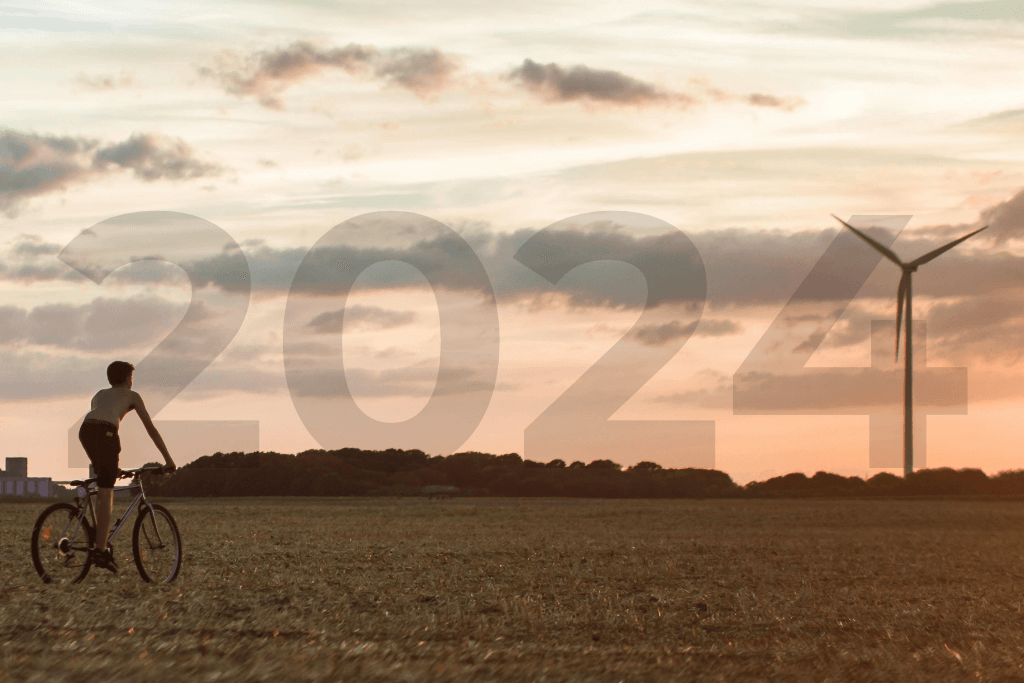 Um garoto anda de bicicleta em direção a uma turbina de energia eólica, ao fundo vemos o número 2024.